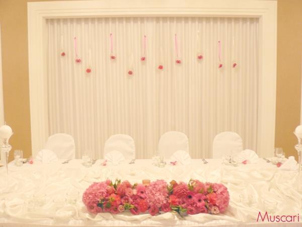 dekoracja stołu pary młodej - malinowa kompozycja kwiatowa i tło za parą młodą