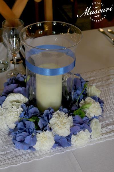 niebieskie kwiaty hortensji i białych goździków w wianku okalającym lampion na stole
