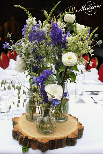 kwiaty na weselnym stole w stylu naturalnym, białe eustomy, róże i niebieskie ostróżki na drewnianych krążkach