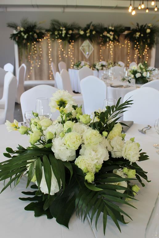 pastelowe kwiaty i egzotyczne liście jako dekoracja stołu na wesele