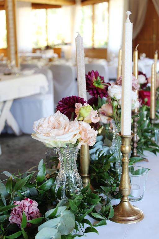 świeczniki, kwiaty i zielona girlanda jako dekoracja stołu pary młodej
