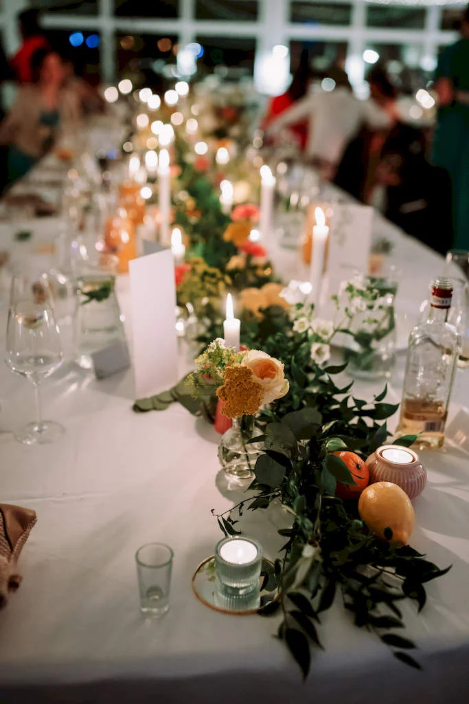 girlanda z kwiatów i zieleni oświetlona światłem świec - dekoracja podłużnego stołu na weselu